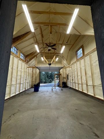 Person in protective gear sprays foam insulation onto a wall in a building.