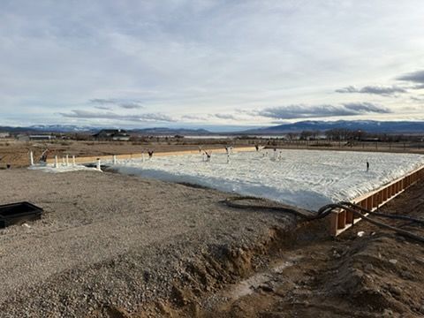 Construction site with a rectangular foundation, insulation, and plumbing, with mountains in the background.