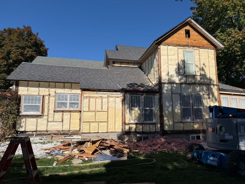 Construction worker installing insulation, wearing a mask and helmet, in a wood-framed structure.