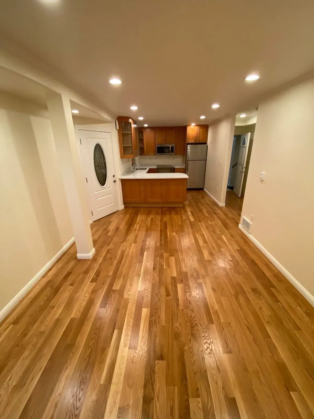 A living room with hardwood floors and a kitchen in the background.