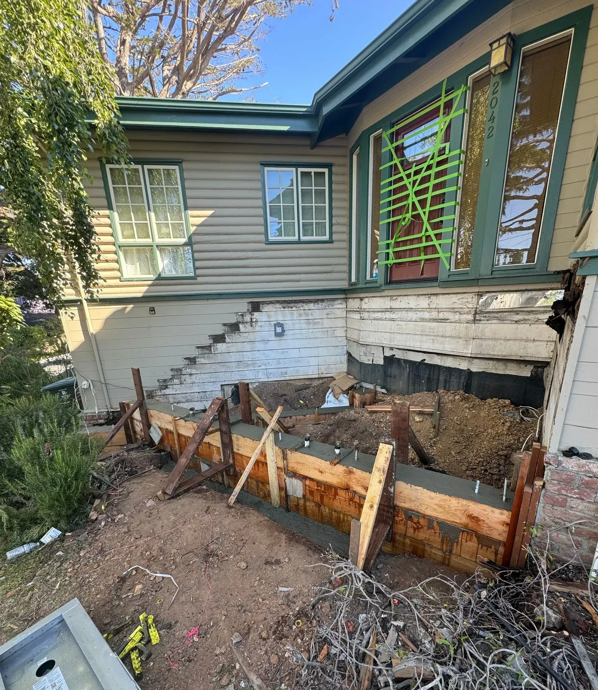 A house is being remodeled and a concrete foundation is being poured in front of it.