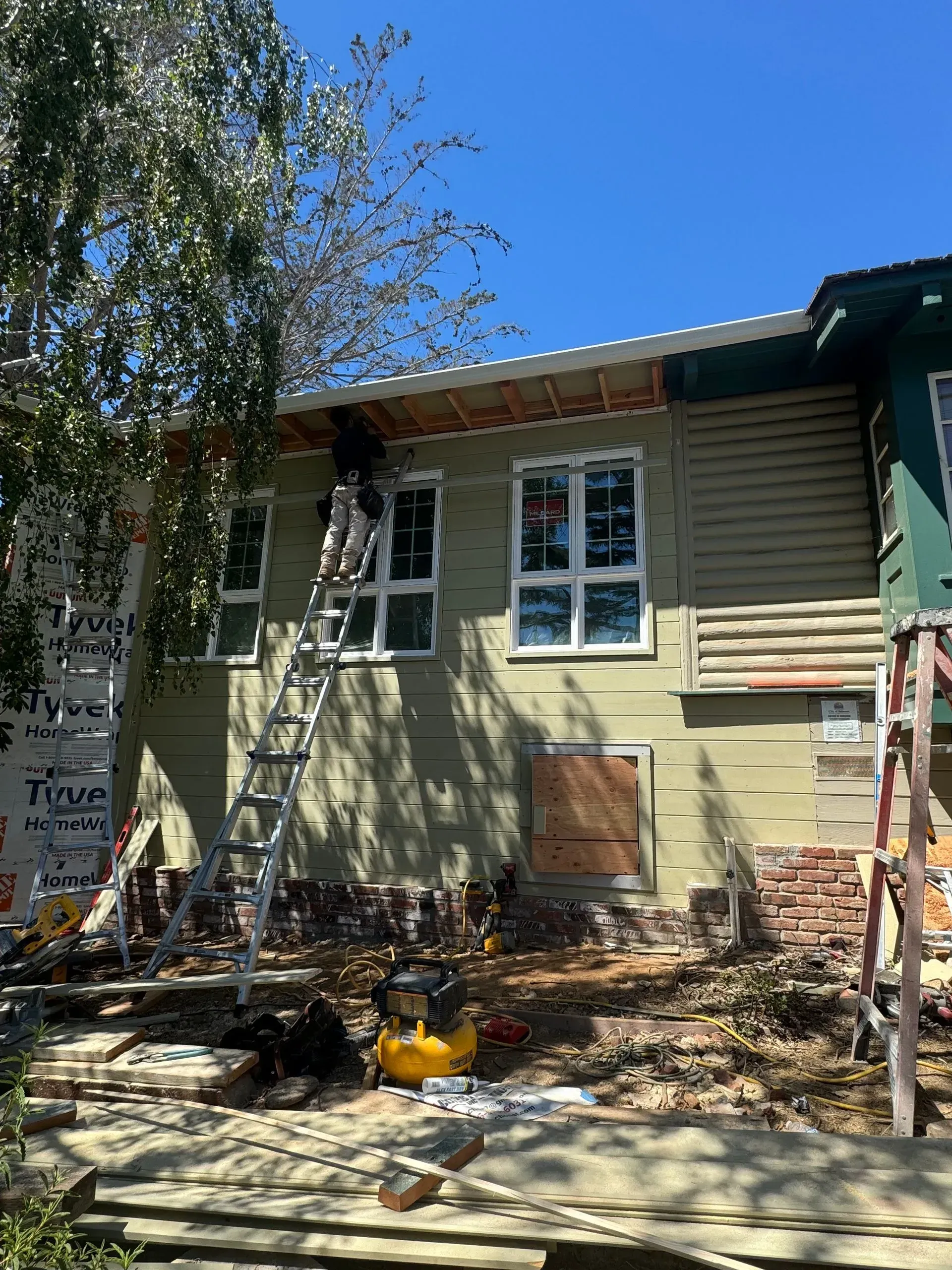 A man is standing on a ladder on the side of a house.