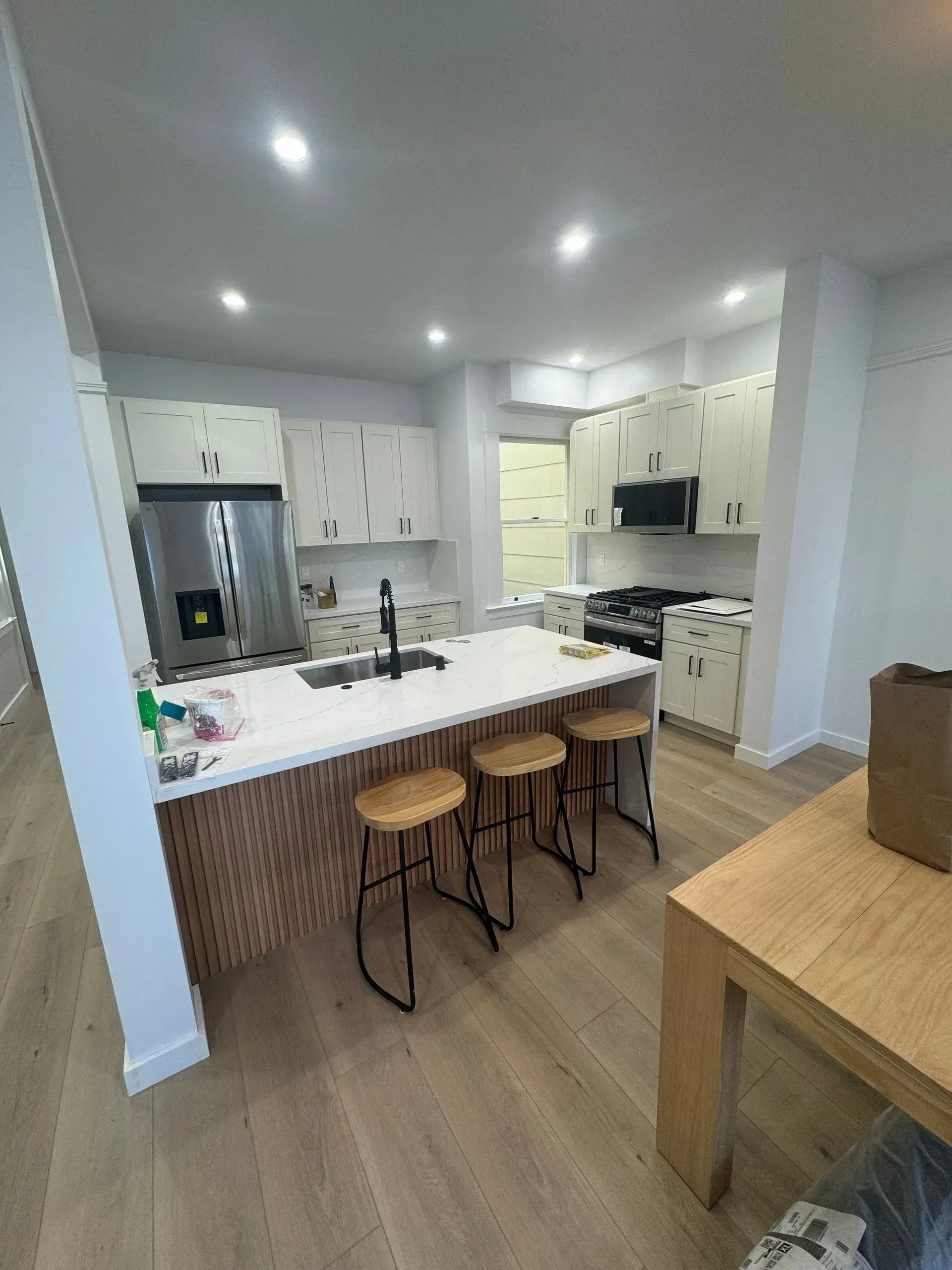 Modern kitchen with white and wood cabinets, an island with stools, and a table.