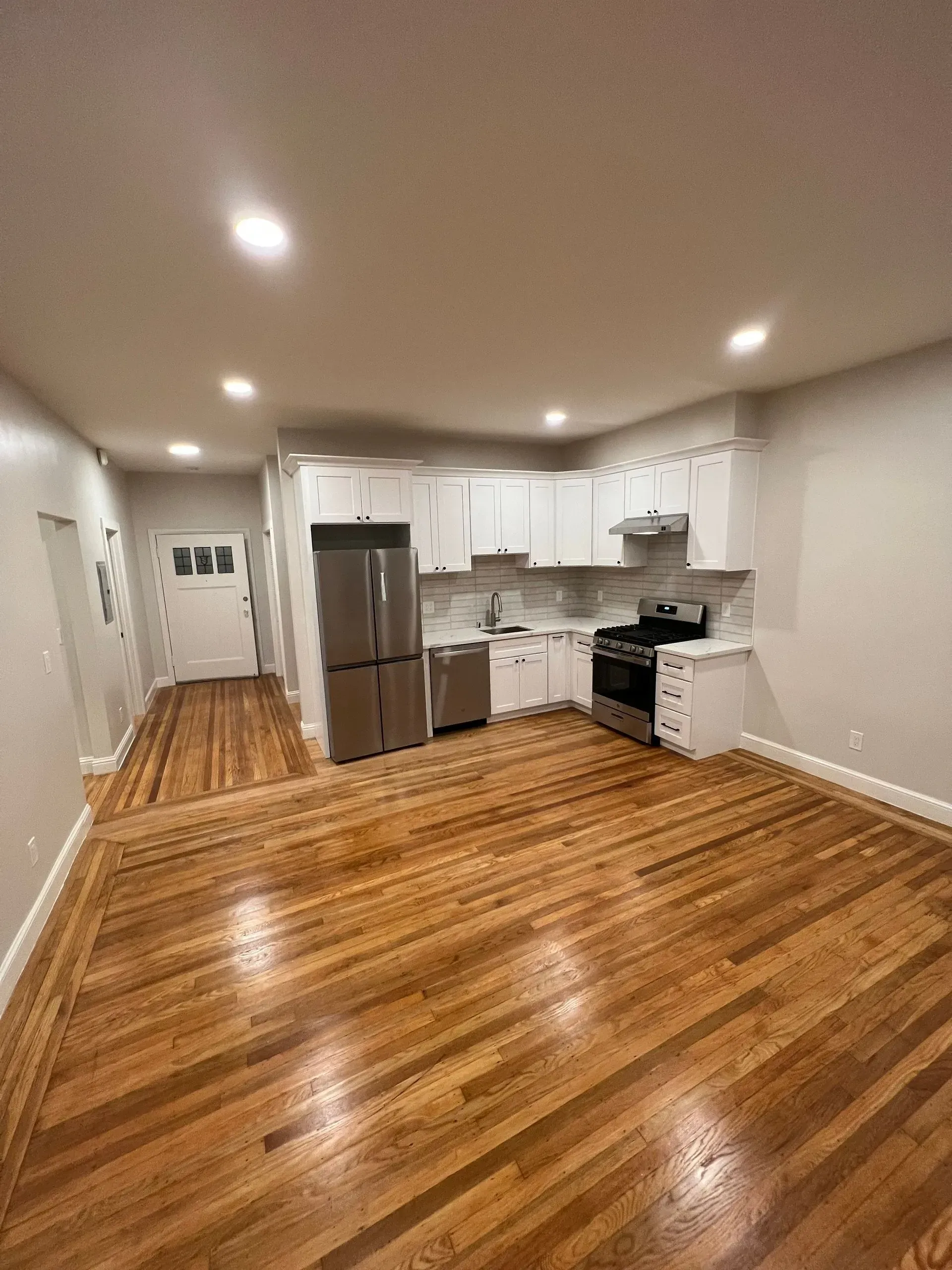 A kitchen with stainless steel appliances and hardwood floors in an empty apartment.