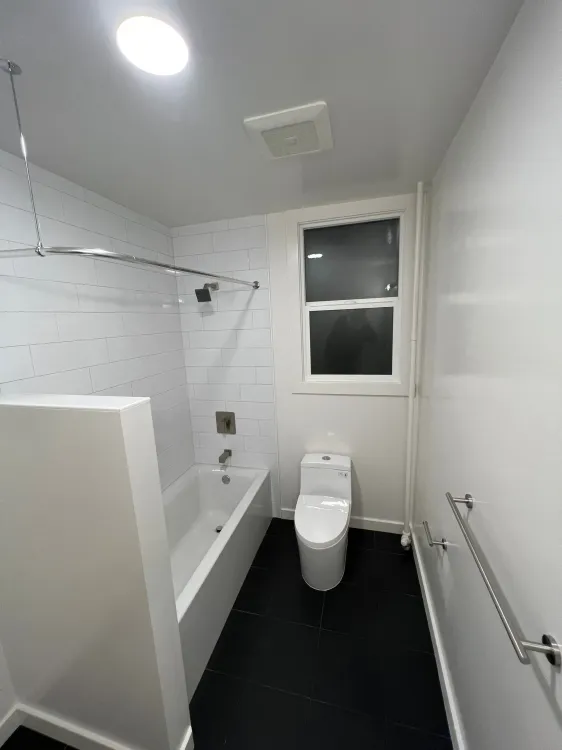 A bathroom with a toilet , tub , shower and window
