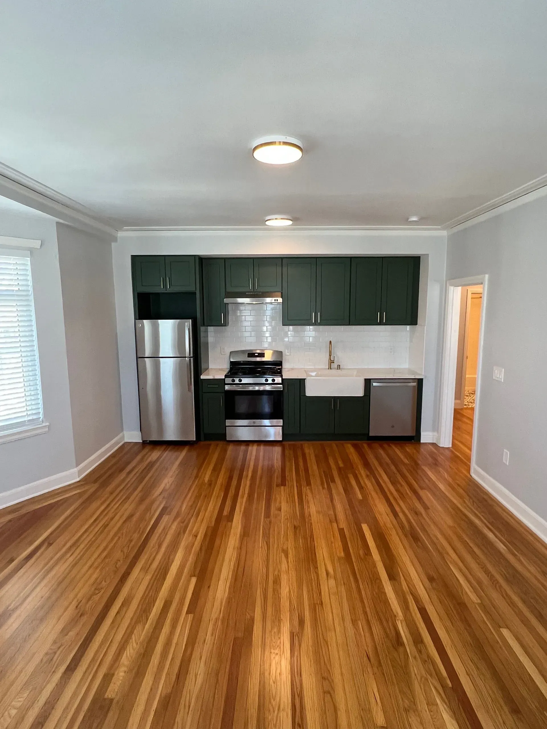 A kitchen with stainless steel appliances and wooden floors in an empty apartment.