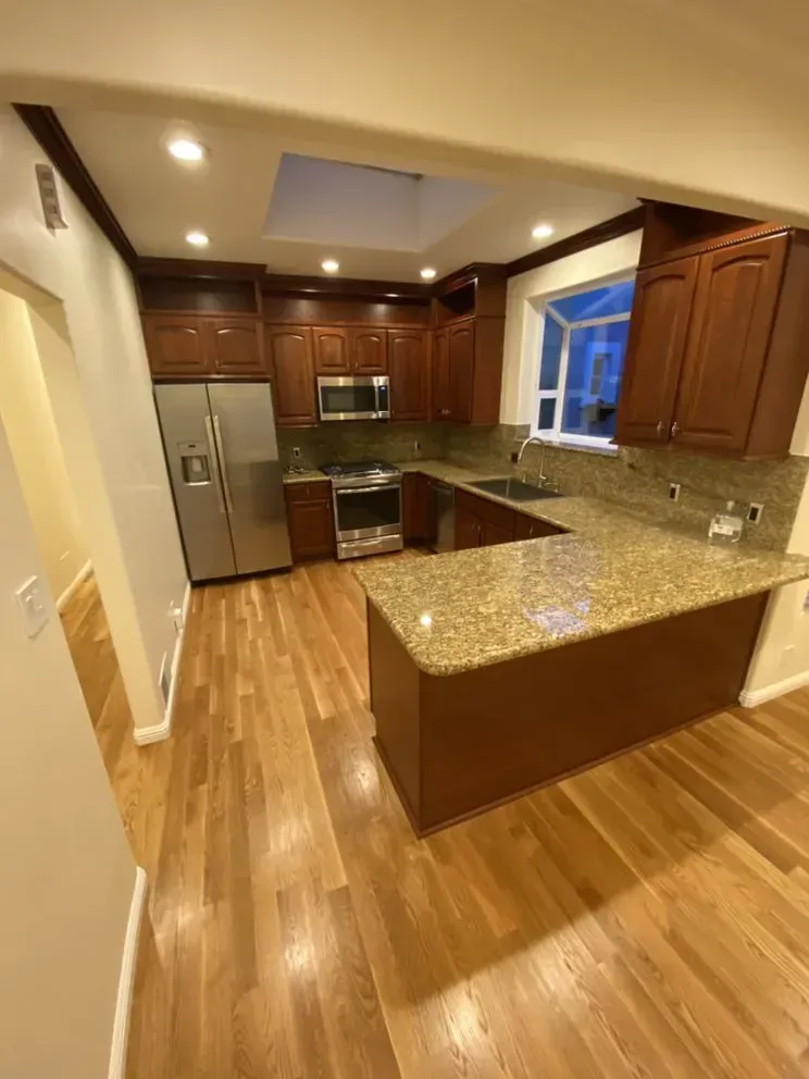 A kitchen with stainless steel appliances , granite counter tops , wooden cabinets and hardwood floors.