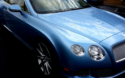 Blue Bentley car, with reflective surface, in a parking area.