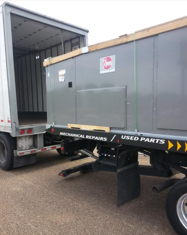 Gray industrial unit on a flatbed trailer being unloaded from a semi-truck. Trailer has 