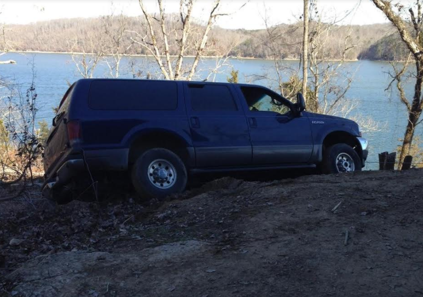 Blue SUV parked on a dirt hill overlooking a lake.
