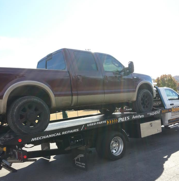 A maroon pickup truck on a tow truck, parked on a sunny day.