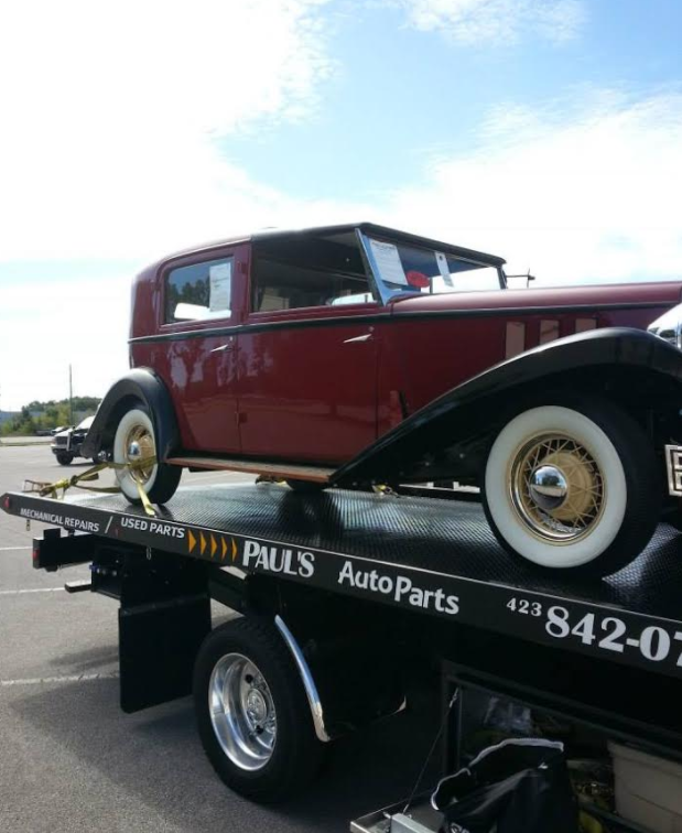 Vintage maroon car on a tow truck, against a blue sky.