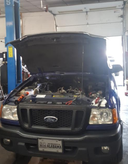 Blue Ford Ranger truck with hood open in a repair shop.