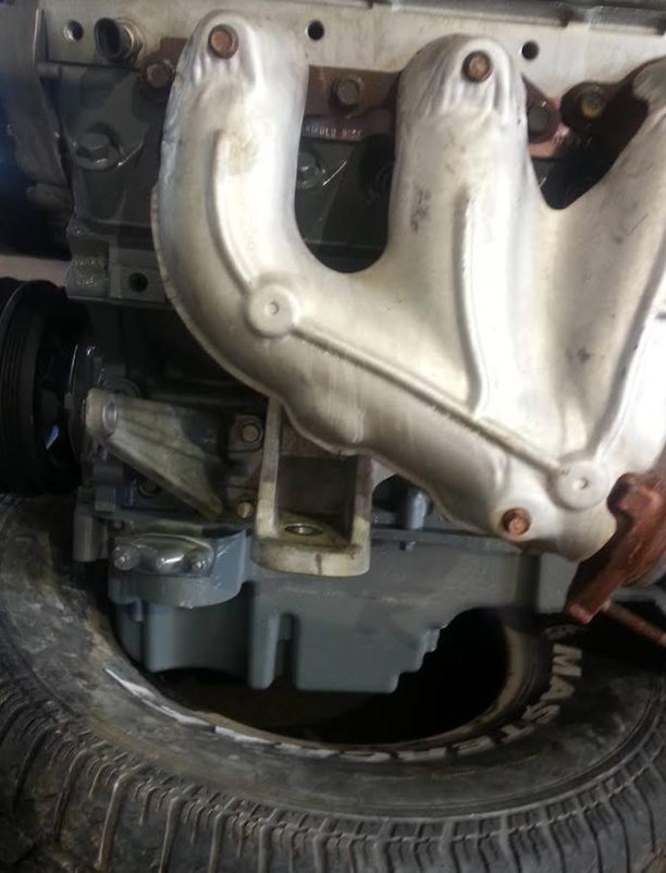 Gray engine block with silver exhaust manifold. Tire rests below the engine.