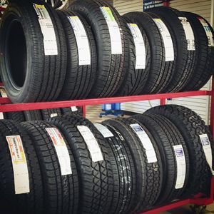 Tires displayed on red metal shelving in a tire shop, with white price tags attached.