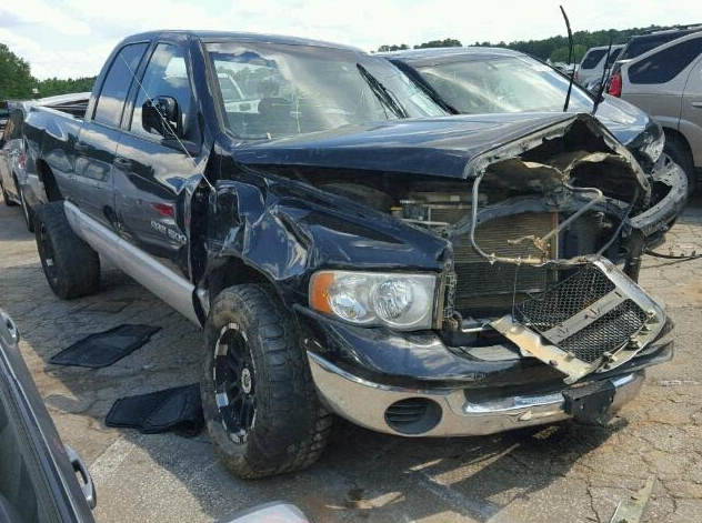 Damaged black Dodge Ram truck with significant front-end collision damage in a salvage yard.