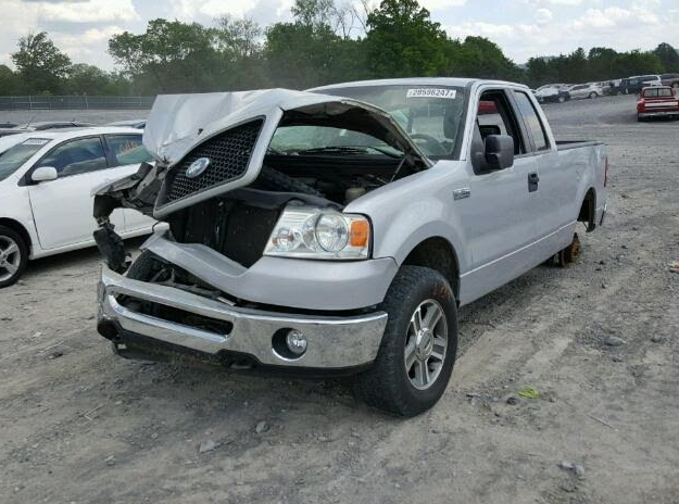 Silver Ford F-150 pickup truck with extensive front-end damage; appears to be in a salvage yard.
