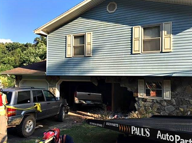 A vehicle crashed into a house's garage, causing damage. A tow truck is present.