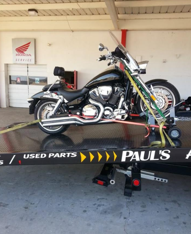 Black motorcycle secured on a tow truck, parked in front of a Honda service shop.