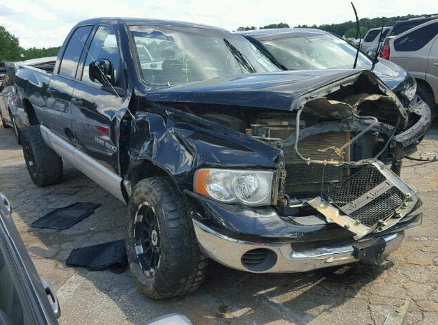 Damaged black Dodge Ram pickup truck with front-end collision damage in a salvage yard.