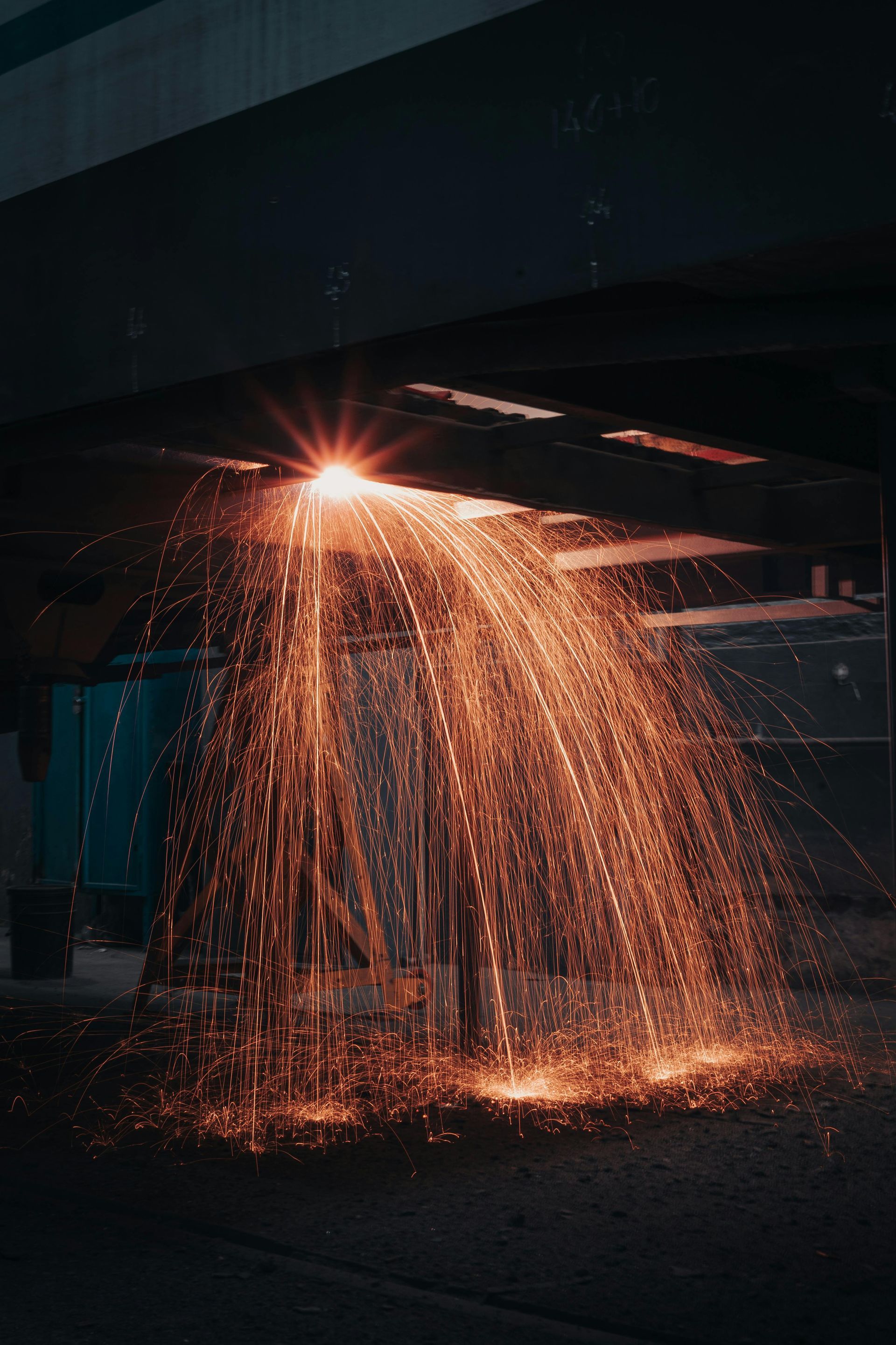 A skilled welder in a protective suit working on metal fabrication, generating a shower of sparks during the welding process.