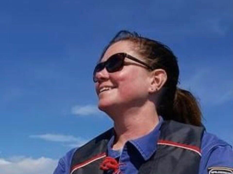 A woman wearing sunglasses and a blue shirt is standing in front of a blue sky.