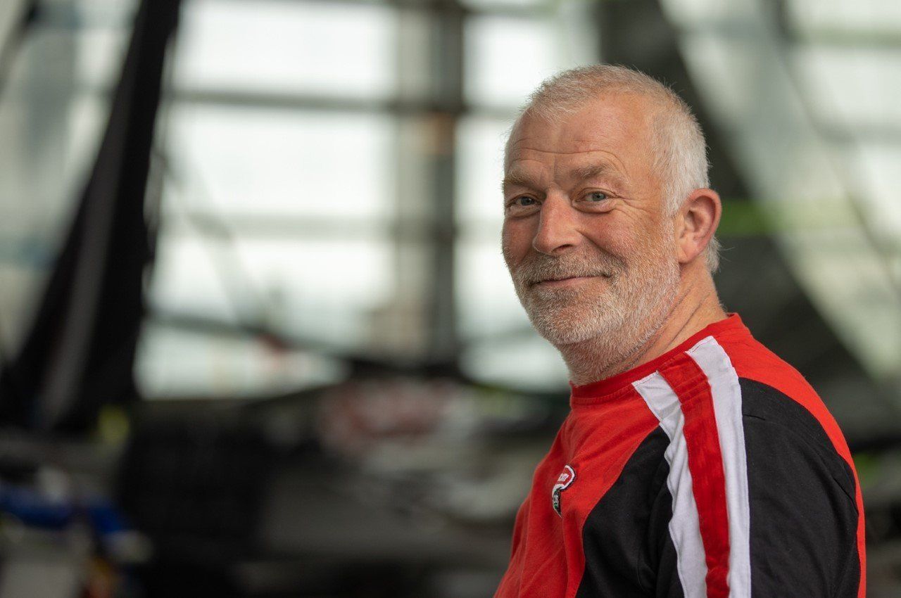 A man with a beard is wearing a red and black shirt and smiling.