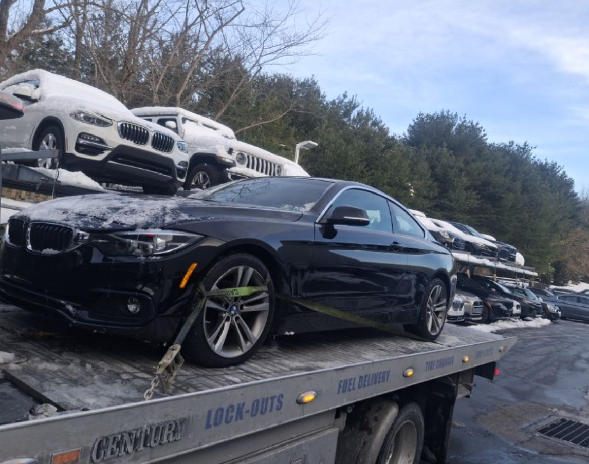 A black car being towed onto a flatbed tow truck on a road, sunny day.