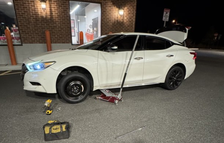 A white car being jacked up for a tire change in a parking lot.