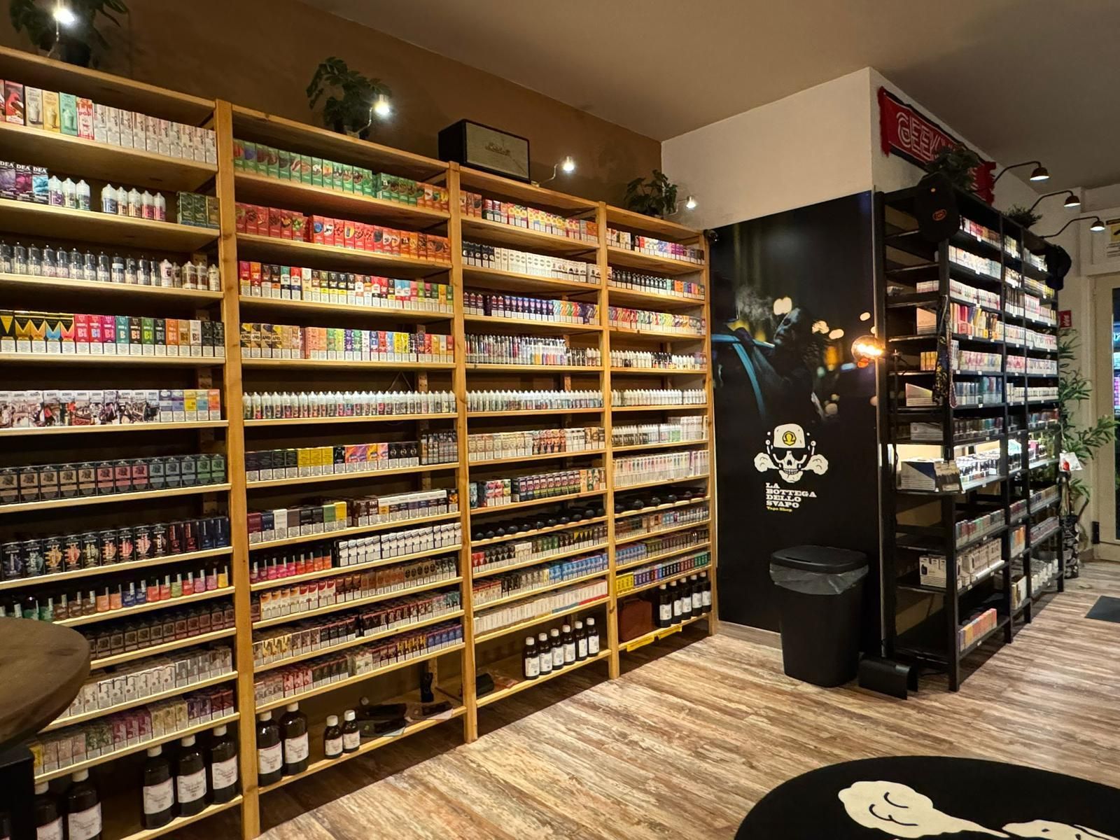 Scaffali pieni di prodotti per lo svapo all'interno di un negozio, con un logo a forma di teschio su una parete.
