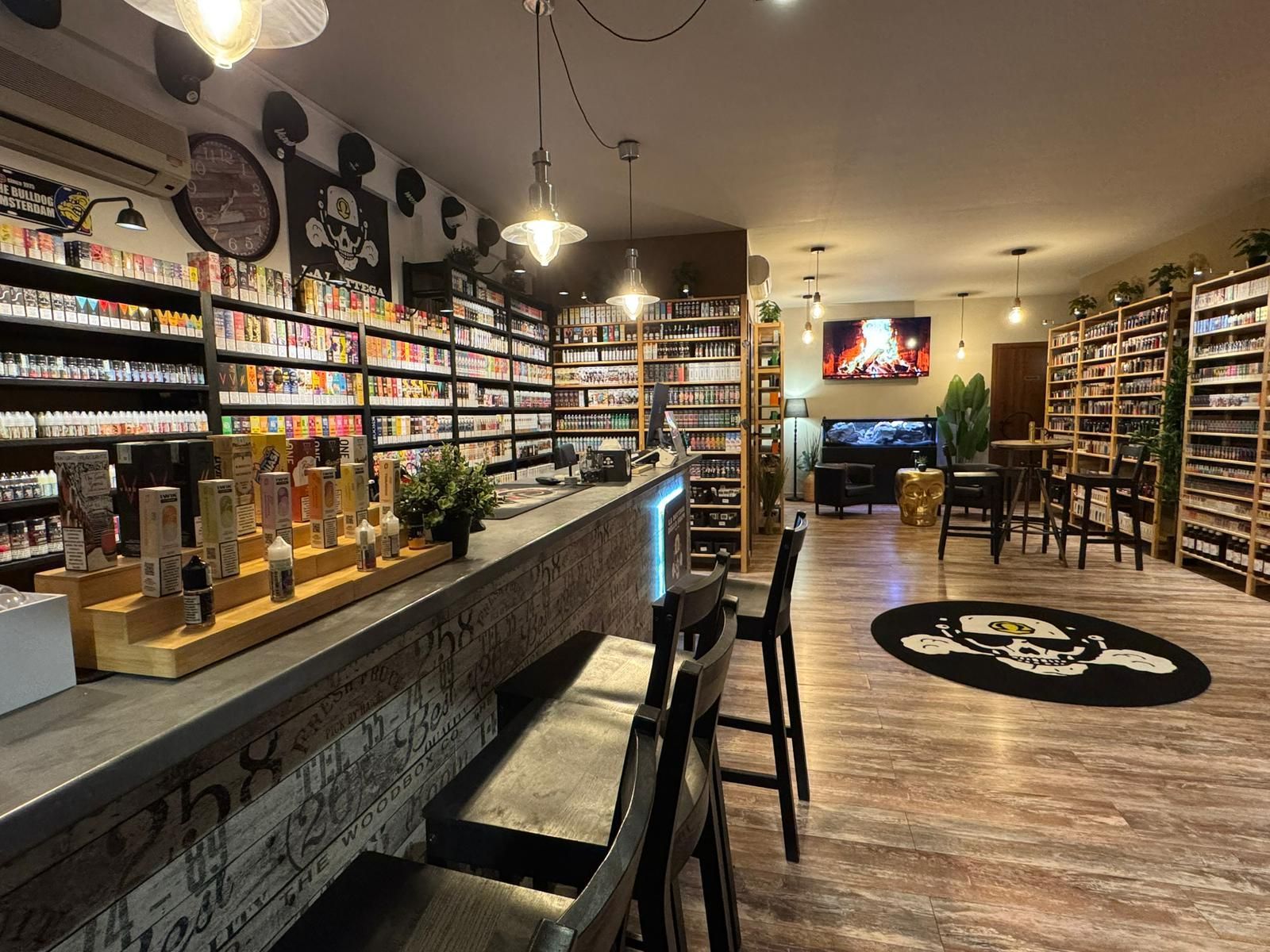 Interno di un negozio di sigarette elettroniche. Scaffali pieni di liquidi per sigarette elettroniche rivestono le pareti, un bar con sgabelli e una TV.