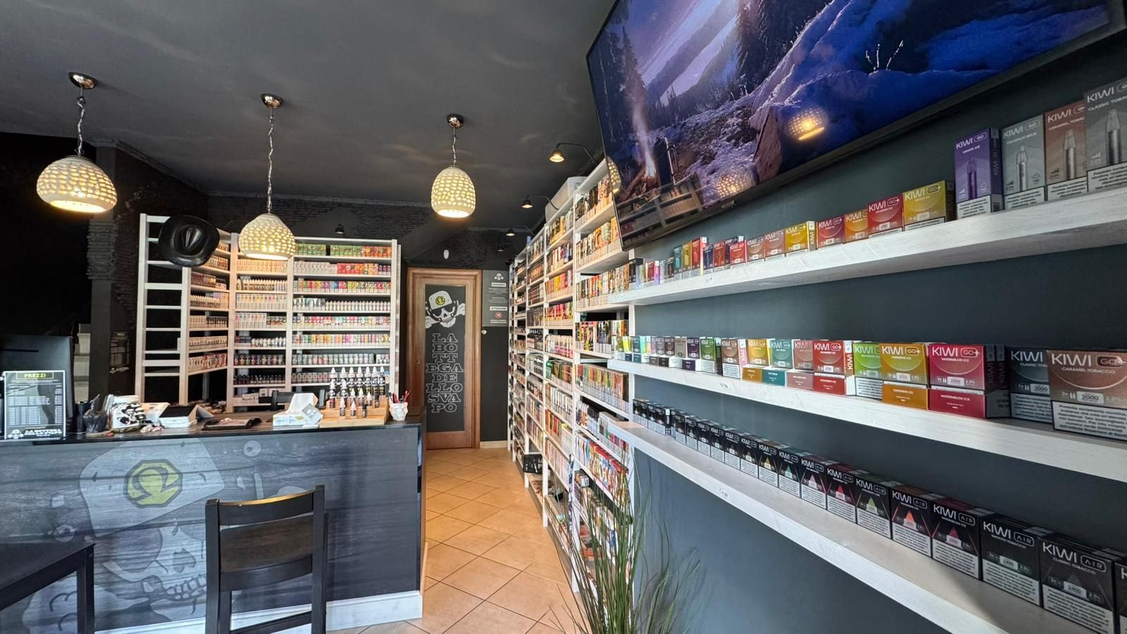 Interno di un negozio di sigarette elettroniche. Scaffali con prodotti per sigarette elettroniche, un bancone e uno schermo TV.
