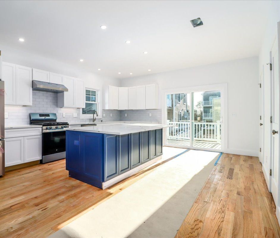 Modern kitchen with blue island, white cabinets, stainless steel appliances, and wooden floors.