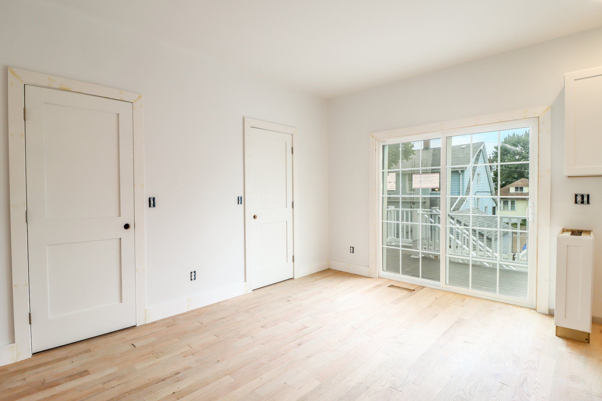 Empty room with wood floors, white walls, two doors, and a sliding glass door with a view of construction.