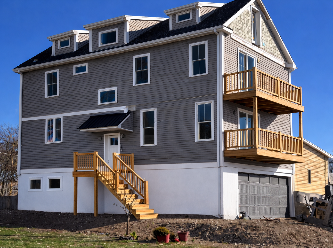 Three-story gray house under construction with multiple windows and a blue sky in the background.