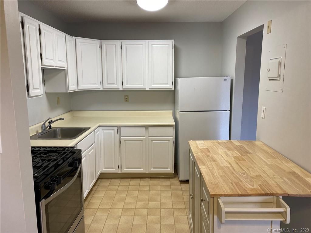 White kitchen cabinets, appliances, and island with a light wooden top.