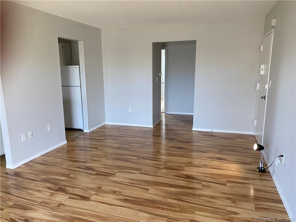 Empty room with wood floors and gray walls. Refrigerator in the kitchen entrance, doorway leading to another room.