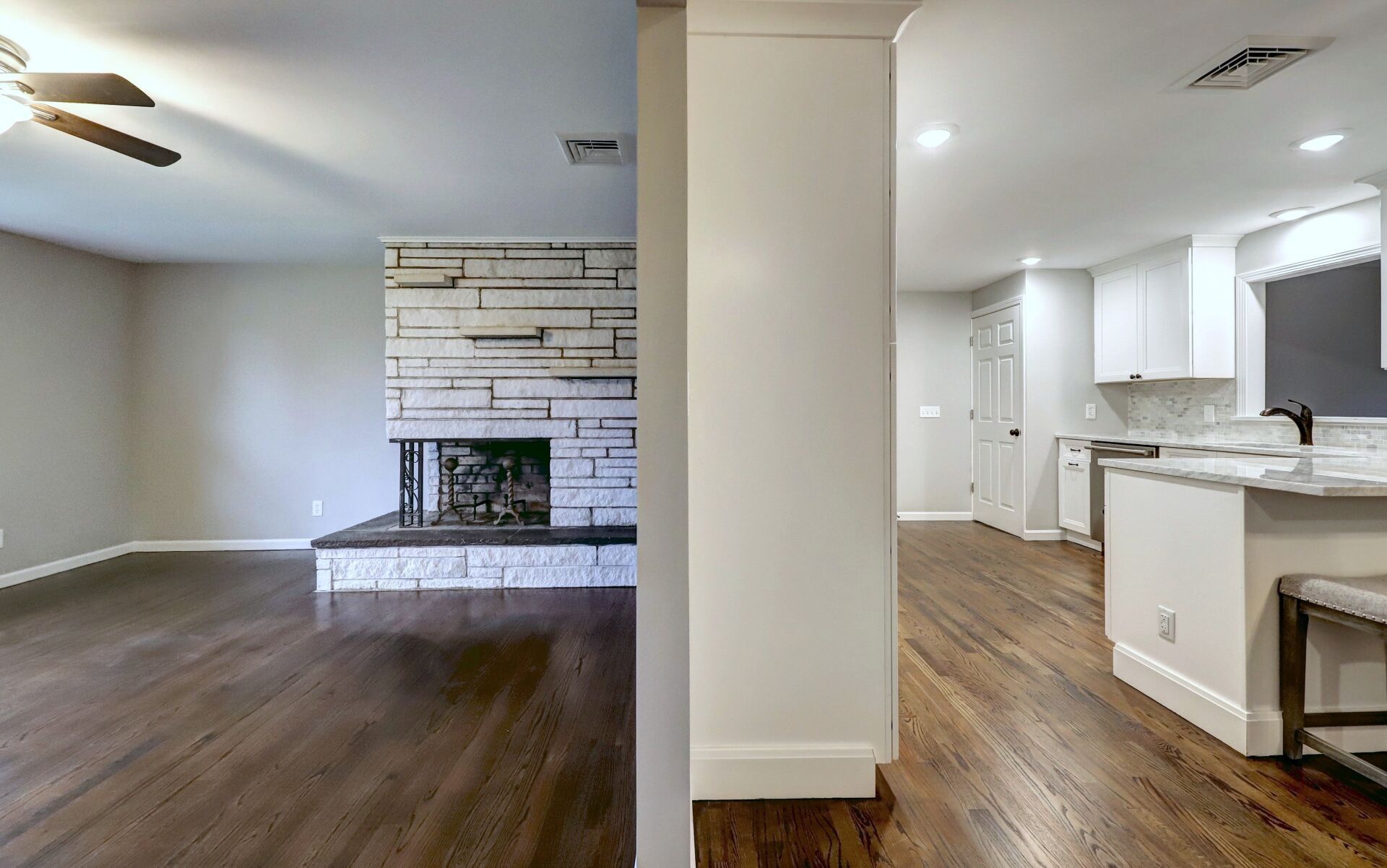 Living room with fireplace, open to kitchen; hardwood floors, neutral walls.