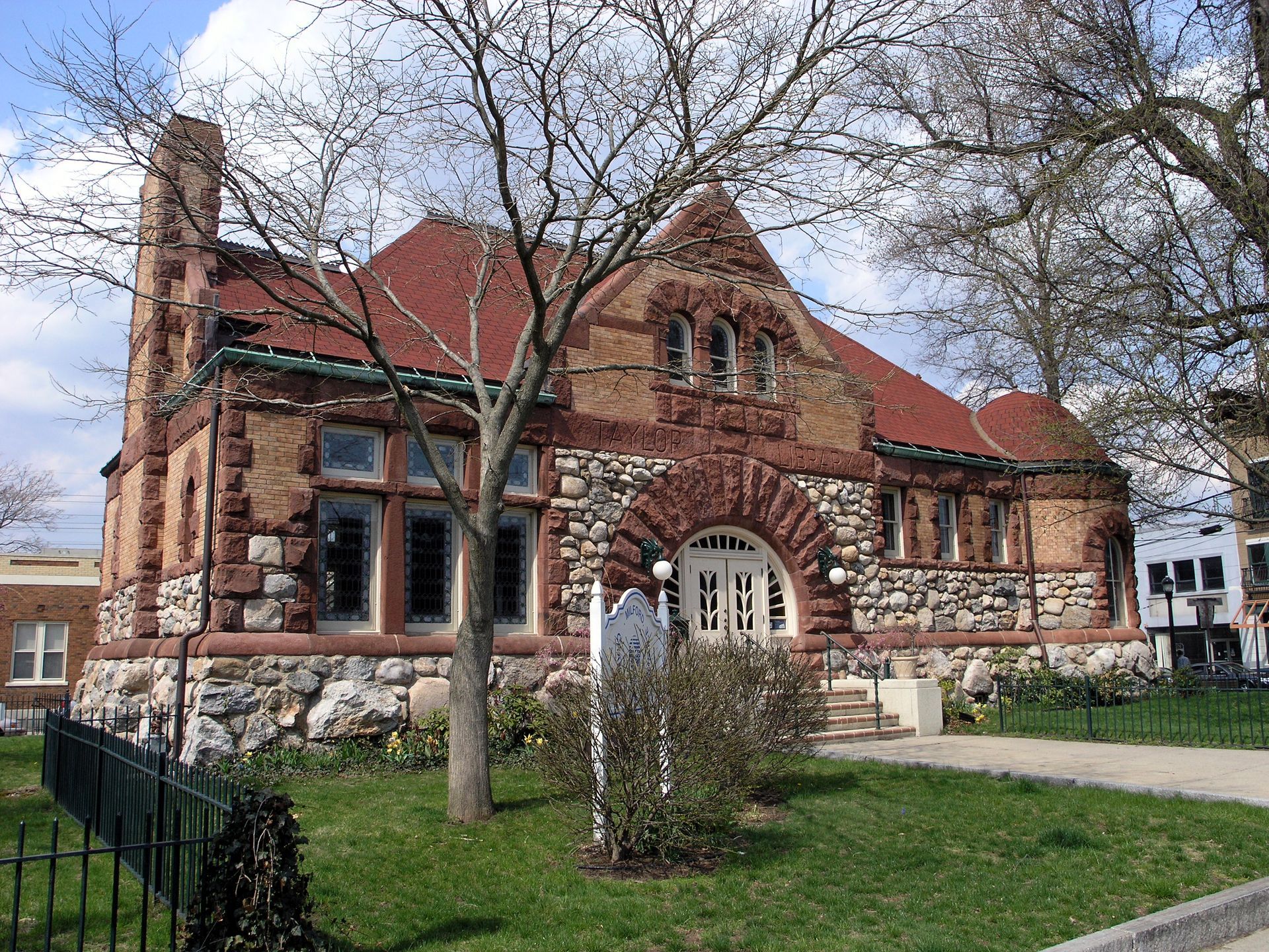 A brick building with stone foundation and red tile roof, in a grassy setting.