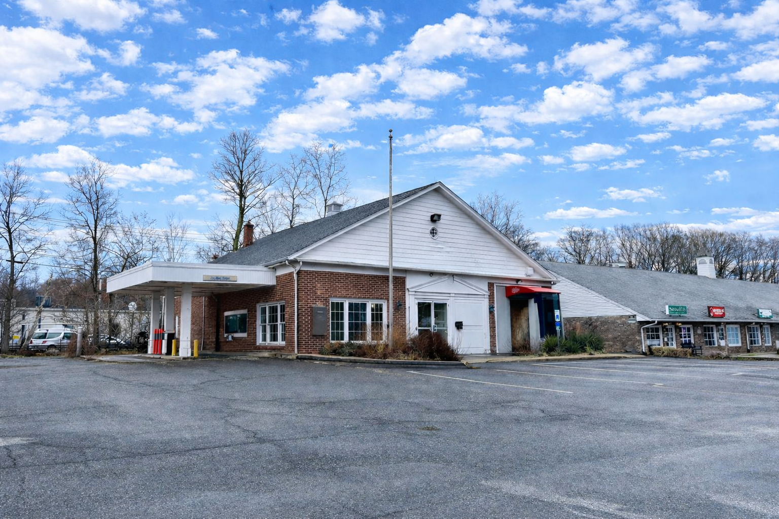 A single-story brick building with a gas pump overhang. Cloudy day. Empty parking lot with traffic cones.