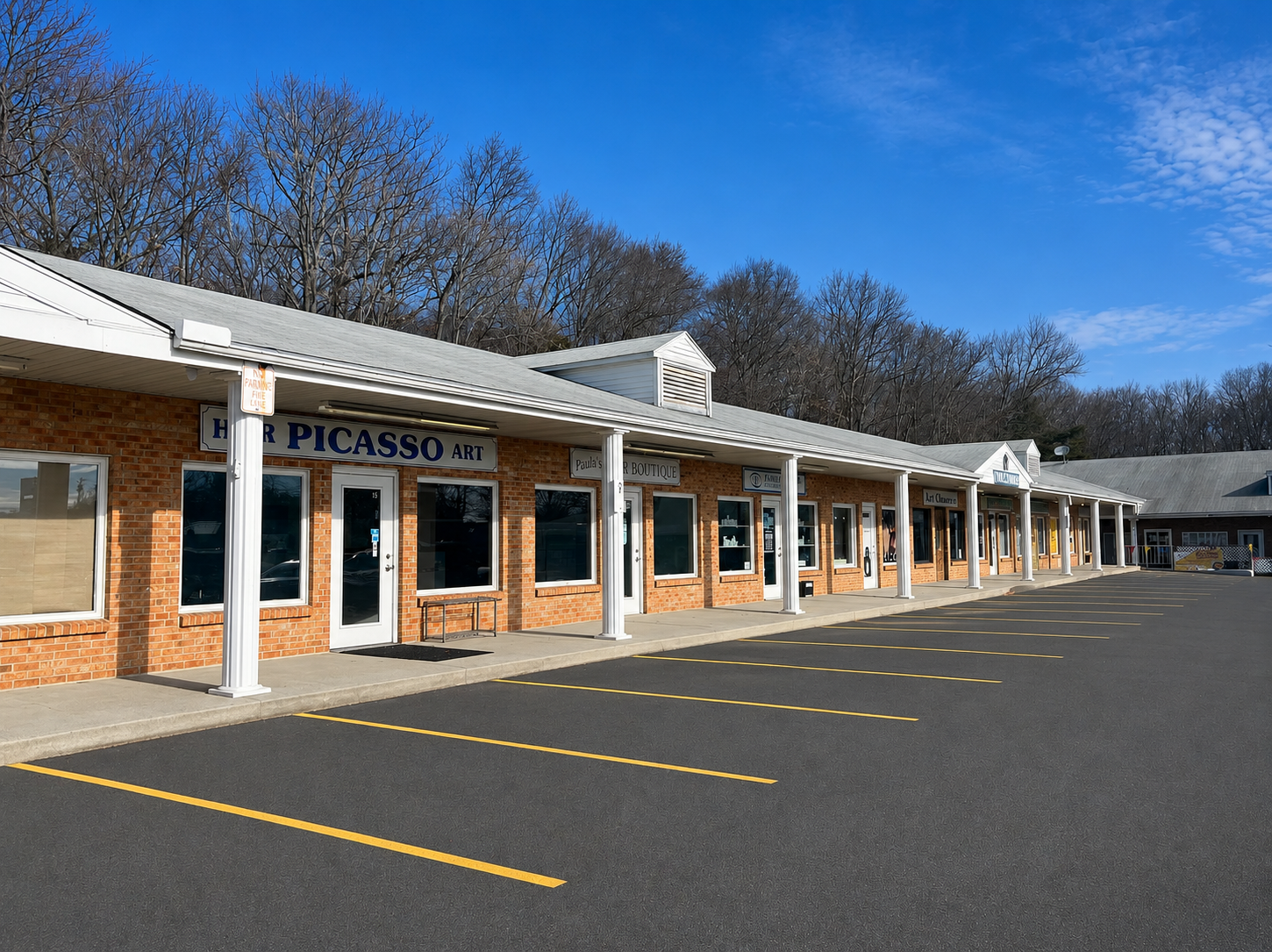 Strip mall storefronts with white awnings and empty parking spaces under a blue sky
