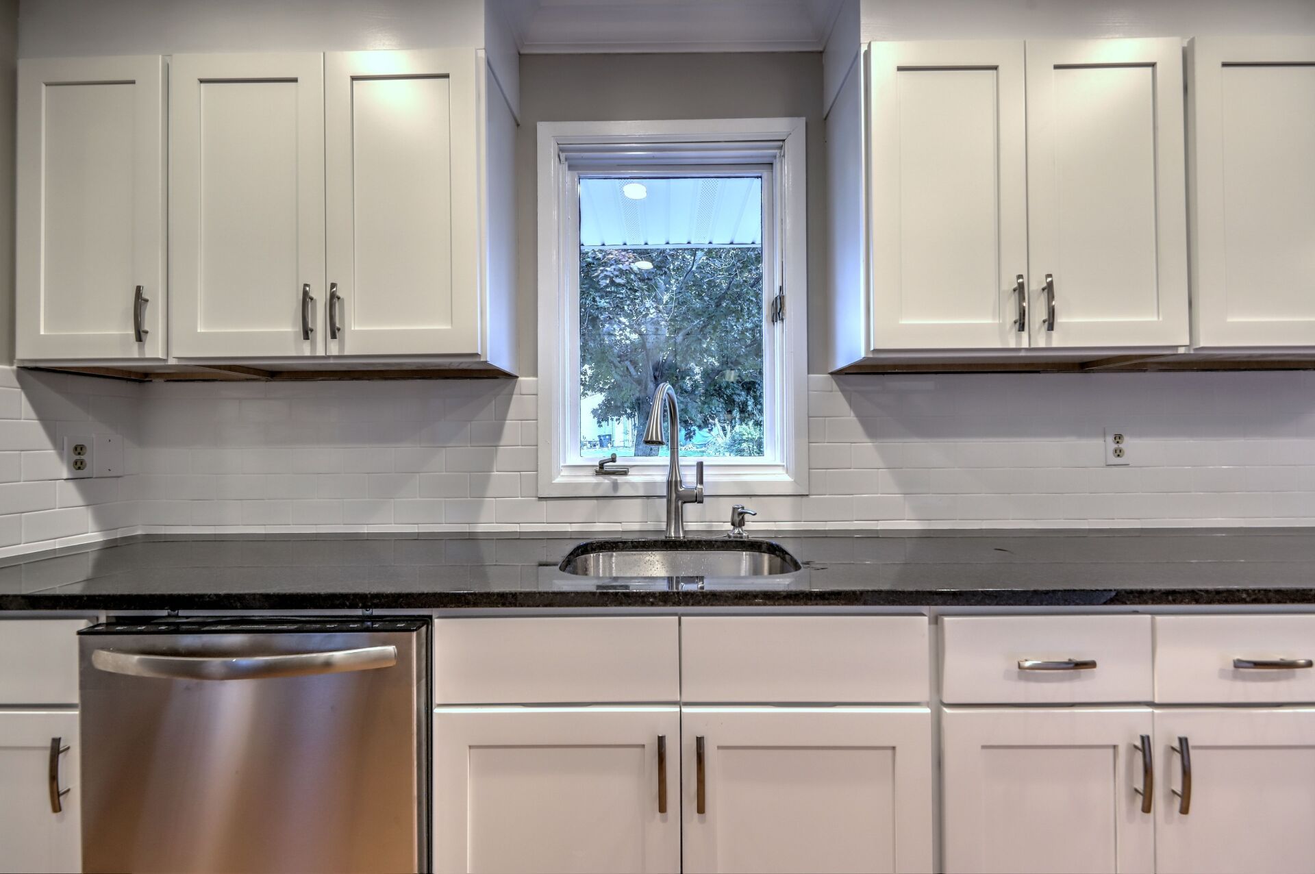 White kitchen cabinets with black countertops, stainless steel appliances, and a window.