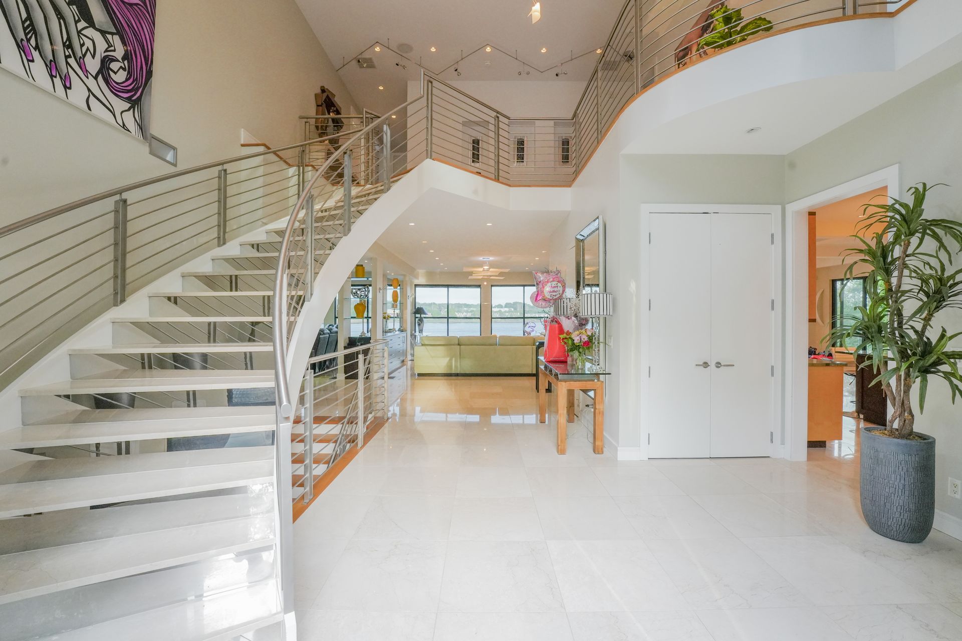 Spacious foyer with a winding staircase, stainless steel railings, and a large plant.