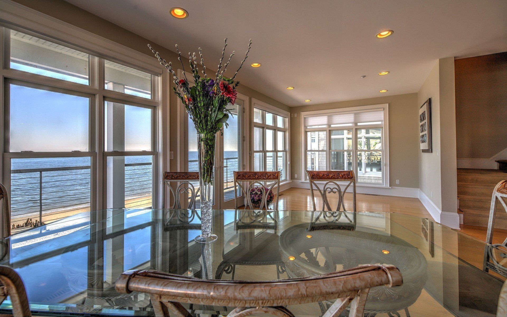 Dining room with a glass table, chairs, and large windows overlooking the water.