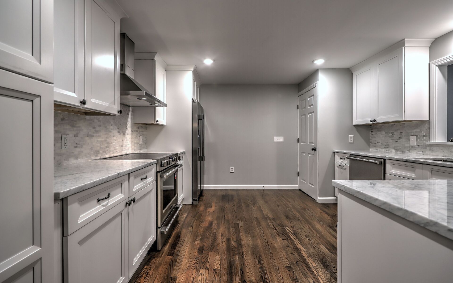 Modern kitchen with white cabinets, stainless steel appliances, and dark wood floors.