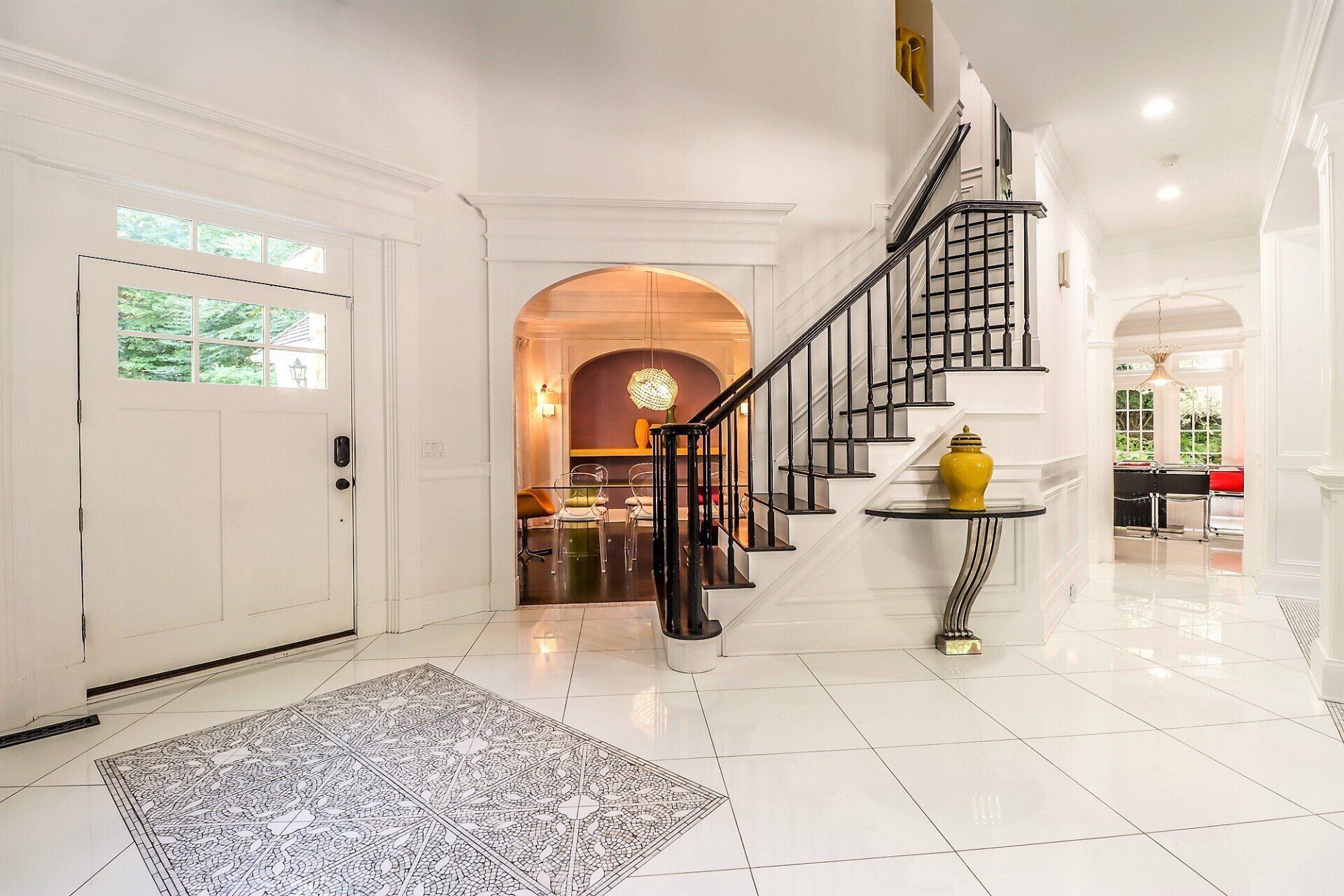 White entryway with a staircase, door, and arched doorway leading to a dining area.