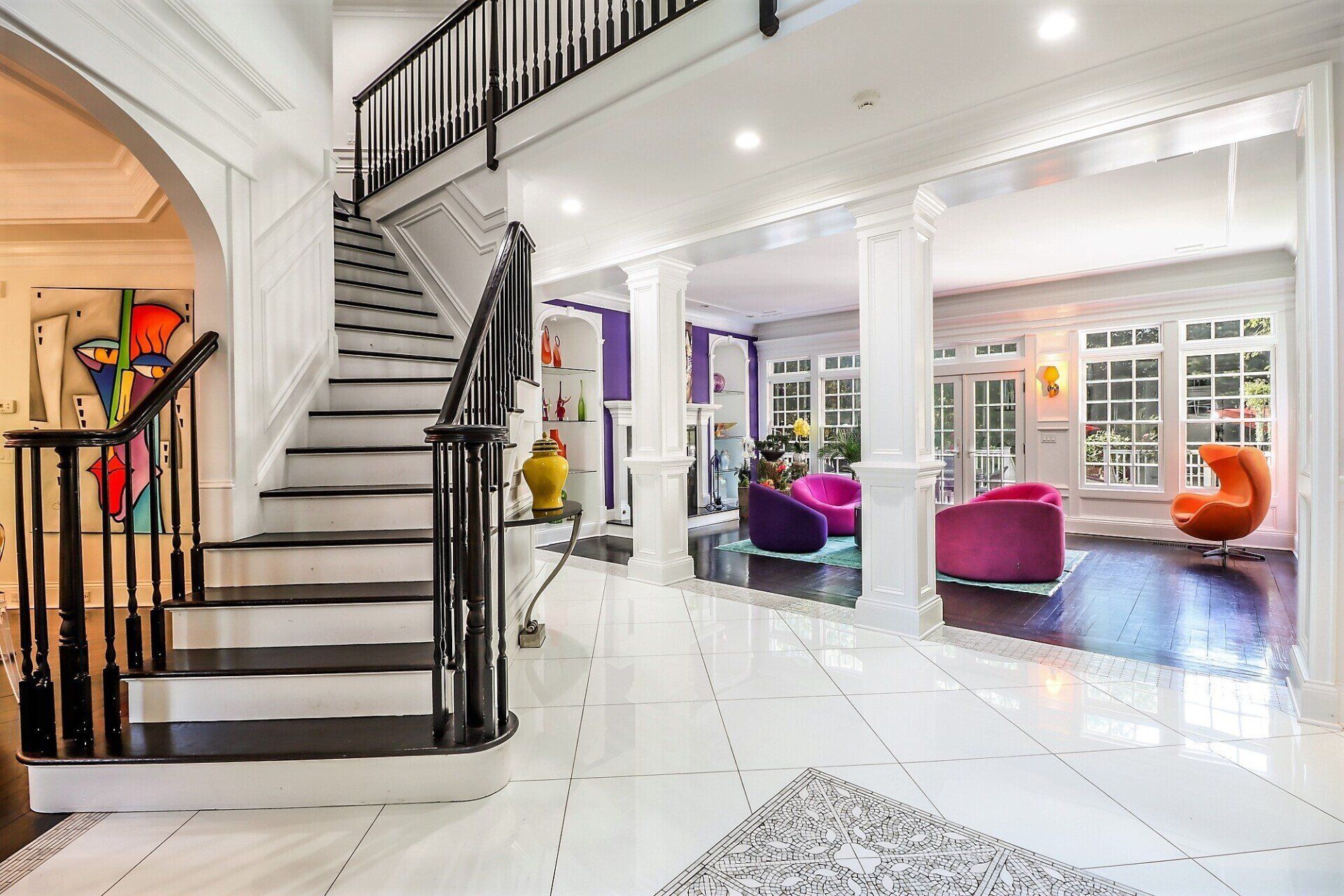 Spacious white foyer with staircase, colorful furniture, and modern art.