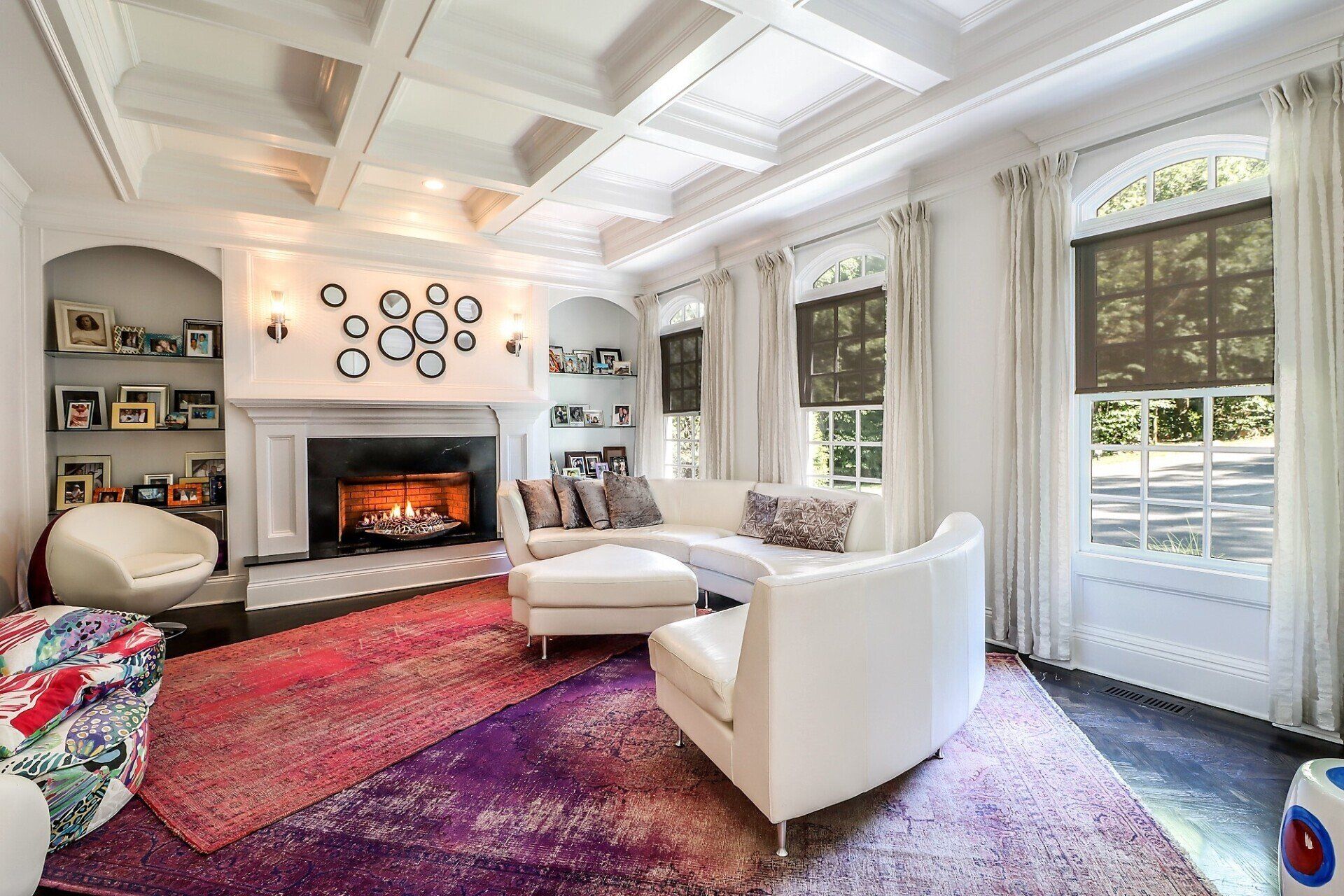 Living room with fireplace, white furniture, colorful rug, and windows.