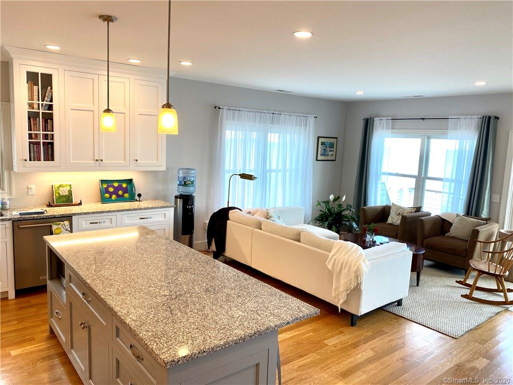 Open-concept kitchen and living room with white cabinets, island, seating, and natural light.