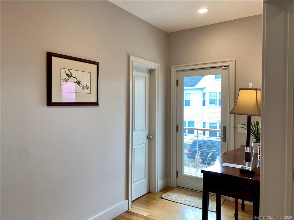 Hallway with framed artwork, white door, and glass door to outside with a small table and lamp.